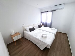 A hotel room with two beds, a bedside table, a lamp, and an air conditioning unit. - 2 bedroom villa | 150m from Praia dos Pescadores | Albufeira (Albufeira)