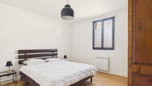 A bedroom with a bed, bedside table, lamp, window, and radiator. - Near the sea, apartment for 2 with terrace (Le Croisic)