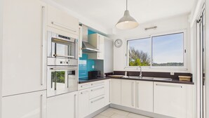 Una cocina moderna con armarios blancos, horno empotrado, microondas, lavamanos y ventana con vistas.