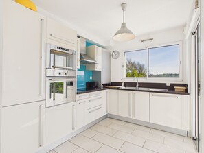 Una cocina moderna con armarios blancos, horno empotrado, microondas, lavamanos y ventana con vistas.