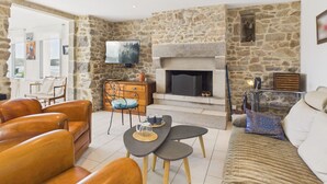 Una sala de estar con paredes de piedra, chimenea, sofás de cuero, una mesa de centro y un televisor montado en la pared.