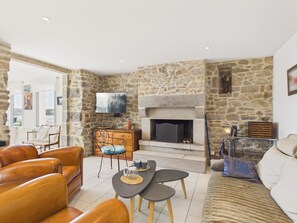 A living room with stone walls, a fireplace, leather sofas, a coffee table, and a television mounted on the wall. - Direct sea access - Charming house for 8 (Plouguerneau)