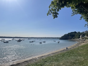Paisatge costaner amb vaixells a l'aigua, una platja i un turó amb edificis.