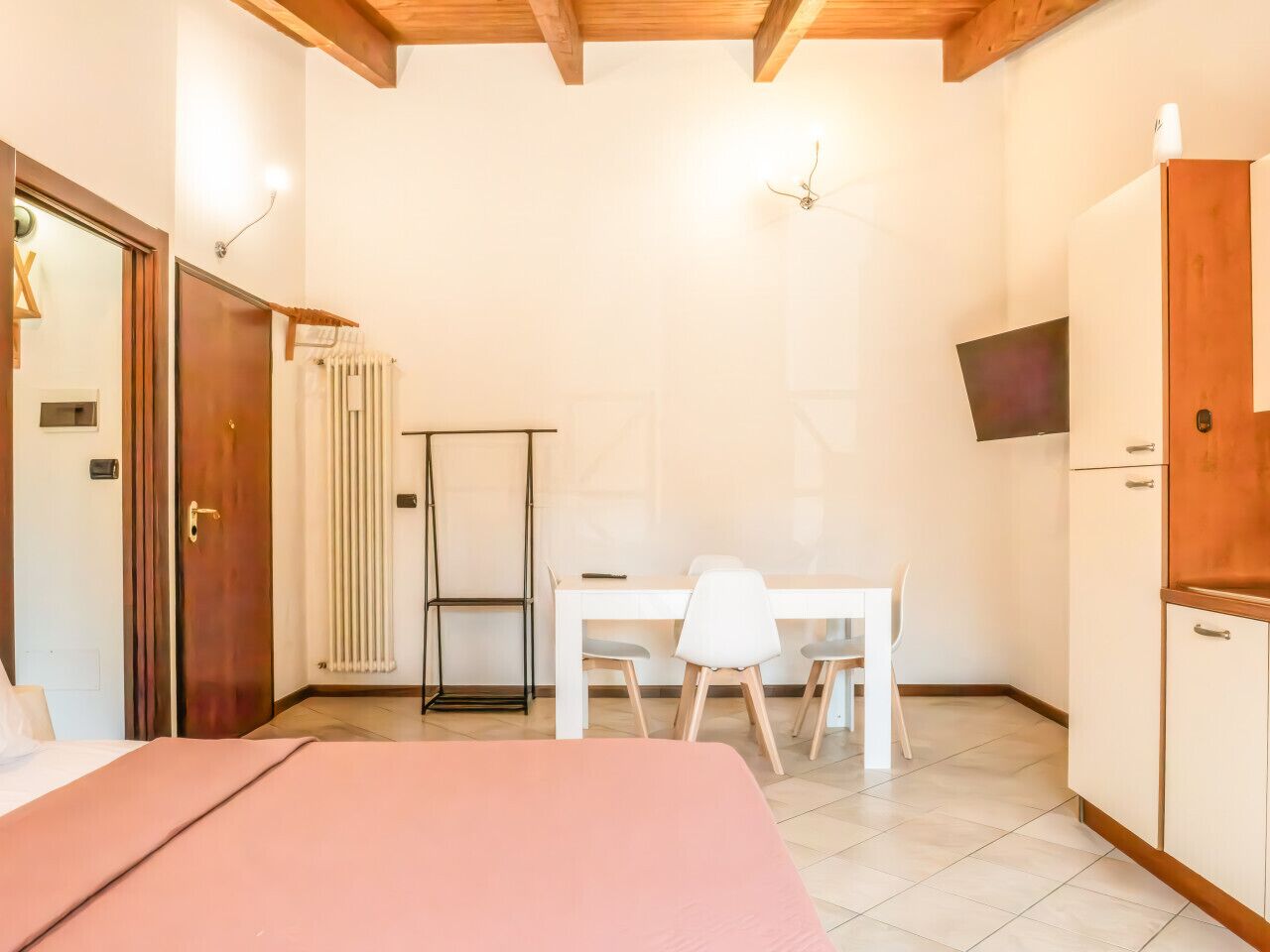 Un dormitorio con cama, un escritorio y una silla. Hay un radiador, un armario y un televisor en la pared.
