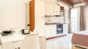 A compact kitchen with white cabinets, a dining table with chairs, a bed, and a window with curtains. - Living 68 - a beautiful loft in Forli (Forlì)