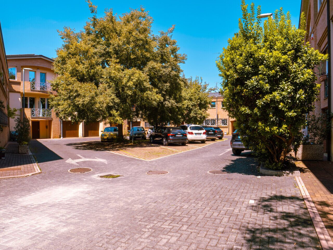 A residential street with parked cars, trees, and buildings.
