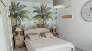 Een slaapkamer met een bed, nachtkastjes, een wandklok en een tropische muurschildering.