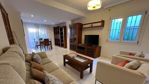 A spacious living room with a sofa set, a coffee table, a TV, and a dining area. - Villa Juani in Playa Los Alamos (Torremolinos)