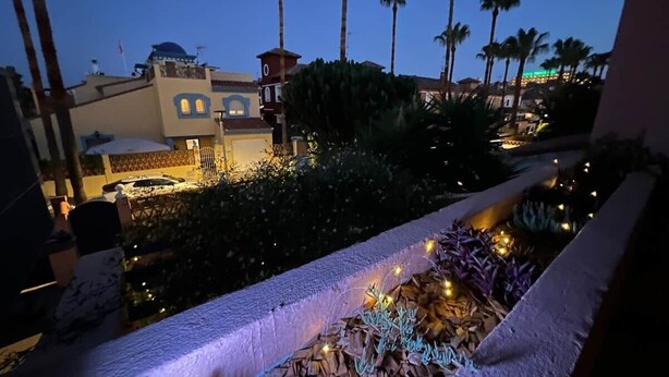 A balcony with a view of palm trees and a building with a clock tower. - Villa Juani in Playa Los Alamos (Torremolinos)