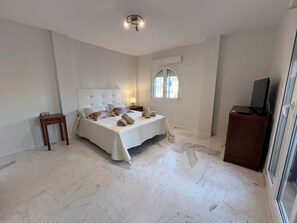 A bedroom with a bed, a bedside table, a window, and a television. - Villa Juani in Playa Los Alamos (Torremolinos)