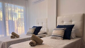 Two twin beds with headboards, a window with blinds, and a rolled towel on each bed. - Villa Juani in Playa Los Alamos (Torremolinos)