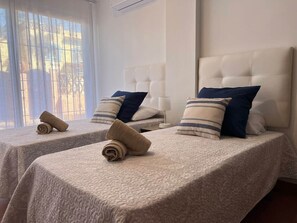 Zwei Einzelbetten mit Kopfteilen, ein Fenster mit Jalousien und auf jedem Bett ein zusammengerolltes Handtuch.