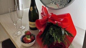 Ett hotellrum med en säng, en spegel, en flaska champagne, två glas, en skål med jordgubbar och en bukett röda blommor.