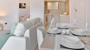 Un soggiorno moderno con zona pranzo, arredi bianchi e una cucina sullo sfondo.