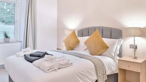 Un letto rifatto con cuscini, una lampada da comodino e vista sugli alberi dalla finestra.