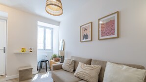 Una sala de estar con un sofá, una mesita, una lámpara, una lámpara de techo de mimbre y dos cuadros enmarcados en la pared.