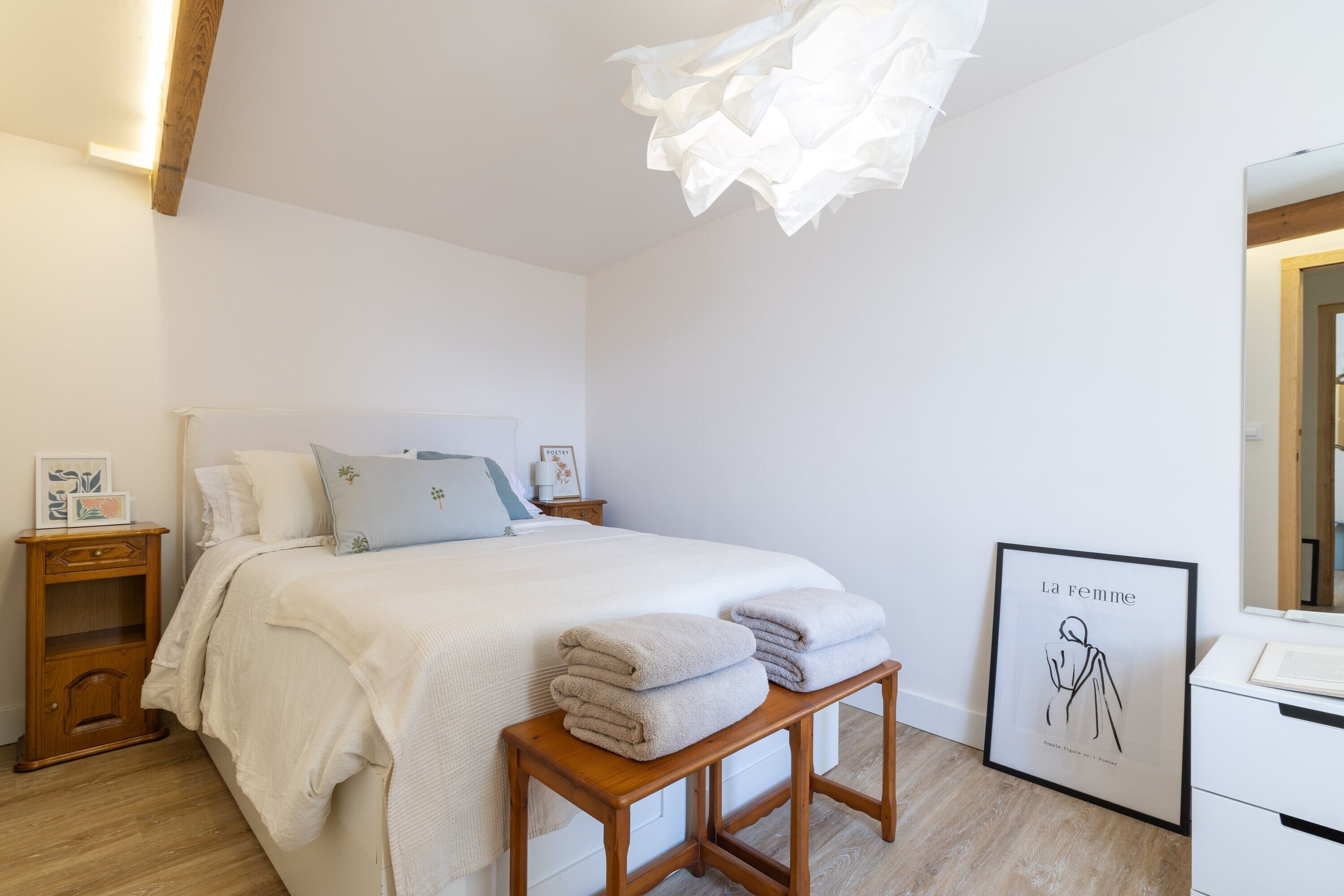 A bedroom with a bed, bedside table, wooden bench, and a framed artwork on the wall.