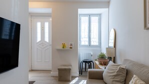 Una sala de estar con un sofá, un televisor, una puerta y una ventana.
