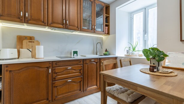 Una cocina con armarios de madera, encimera blanca, un lavabo y una mesa de comedor con sillas.