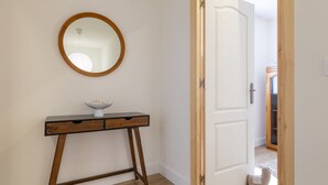Un pasillo con una consola de madera, un espejo redondo y una puerta blanca que da a otra habitación.