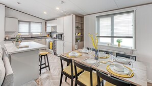 A modern kitchen with a dining area, featuring a central island, built-in appliances, and a window with blinds.