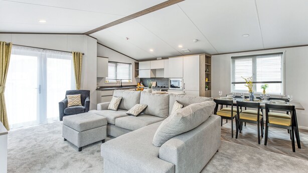 A modern living room with a grey sectional sofa, a small armchair, and a dining table with chairs.