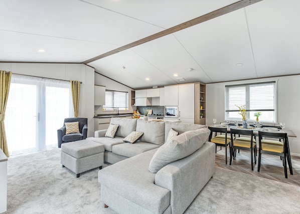 A modern living room with a grey sectional sofa, a small armchair, and a dining table with chairs.