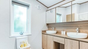 A modern bathroom with a toilet, bidet, two sinks, a large mirror, and a window.