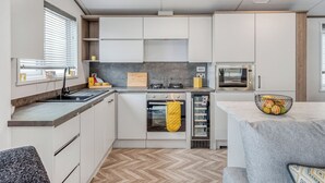 A modern kitchen with white cabinetry, a built-in oven, a microwave, and a dining area with a grey table and a bowl of fruit.