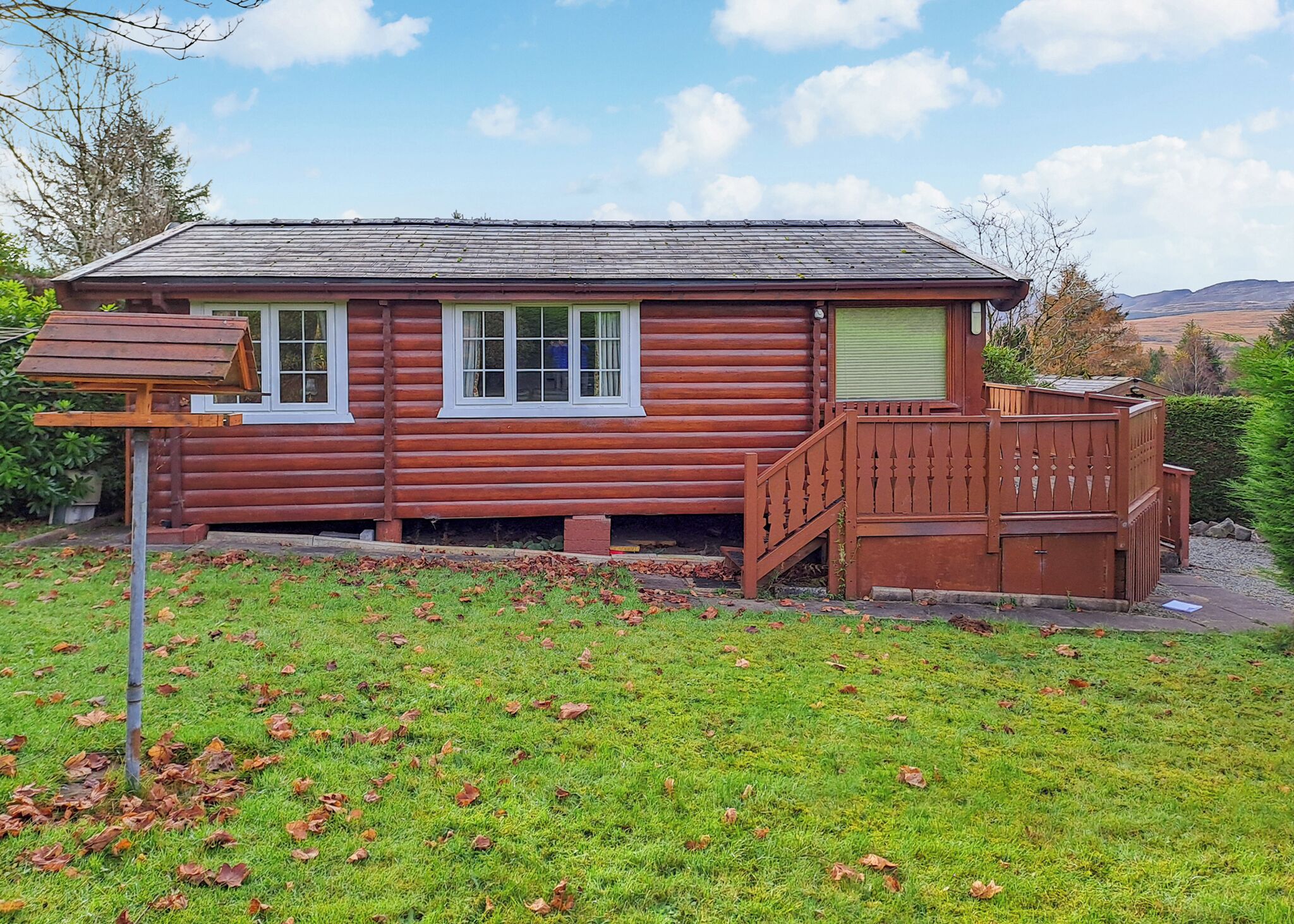 A log cabin with a wooden deck, a small porch, and a grassy yard.