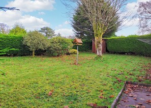 Un jardin bien entretenu, agrémenté d’une mangeoire à oiseaux, de haies soigneusement taillées et de différentes espèces d’arbres.