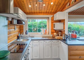Une cuisine aux murs en bois, une fenêtre donnant sur un paysage verdoyant, un évier et une cuisinière.