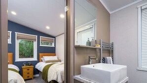 Une chambre avec deux lits, un grand miroir, un lavabo blanc et une fenêtre avec des stores.