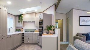 Une cuisine compacte dotée d’appareils électroménagers modernes, d’un plancher à motifs en chevrons et donnant sur un espace de vie avec un canapé et une citation encadrée au mur.