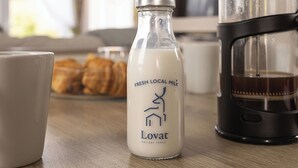 Une bouteille de lait frais provenant d’une ferme locale, une machine à café et une tasse posés sur une table en bois.