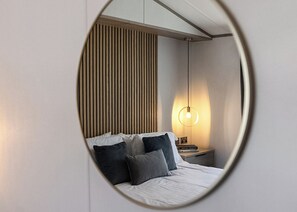 A bedroom with a bed, pillows, a nightstand, a lamp, and a mirror.