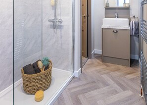A bathroom with a glass shower enclosure, a wooden basket with bath items, and a herringbone-patterned floor.
