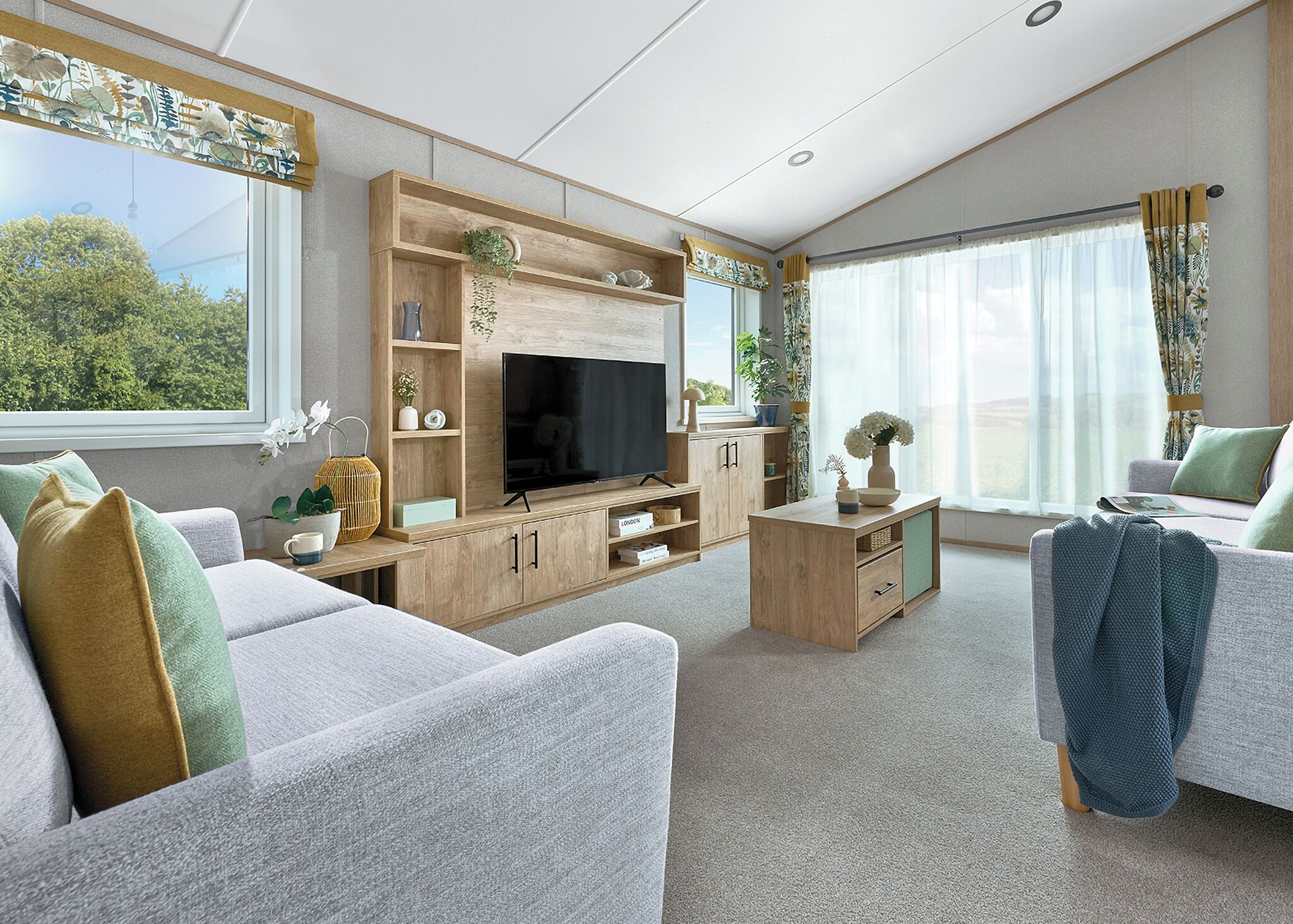 A modern living room with a flat-screen TV, wooden furniture, and large windows with curtains.