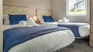A hotel room with two beds, each with a blue quilted bedspread, white linens, and matching blue pillows. There is a window with a view of a house outside. - 1 bedroom accommodation in Mawgan Porth, Nr Newquay (Mawgan Porth, Nr Newquay)