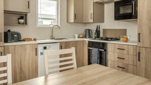 A modern kitchen with a dishwasher, stove, microwave, and a window above the sink. - 1 bedroom accommodation in Mawgan Porth, Nr Newquay (Mawgan Porth, Nr Newquay)