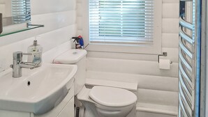 A bathroom with a white sink, toilet, and window with blinds. - 2 bedroom accommodation in Blaenau Ffestiniog (Blaenau Ffestiniog)