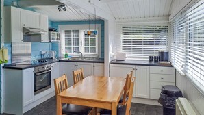 A compact kitchen with a dining table, chairs, a stove, and a window with blinds. - 2 bedroom accommodation in Blaenau Ffestiniog (Blaenau Ffestiniog)