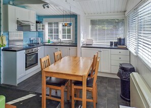 A compact kitchen with a dining table, chairs, a stove, and a window with blinds. - 2 bedroom accommodation in Blaenau Ffestiniog (Blaenau Ffestiniog)