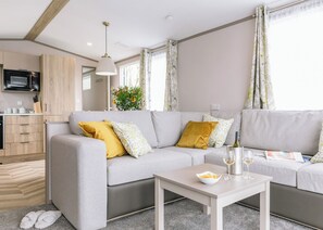 A modern living room with a sofa, a small table, and a kitchen area in the background. - Luxury Plus 2 Bed (Pet) (Mawgan Porth, Nr Newquay)