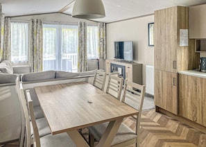 A modern living room with a sofa, a dining table, and a TV. - Luxury Plus 2 Bed (Pet) (Mawgan Porth, Nr Newquay)
