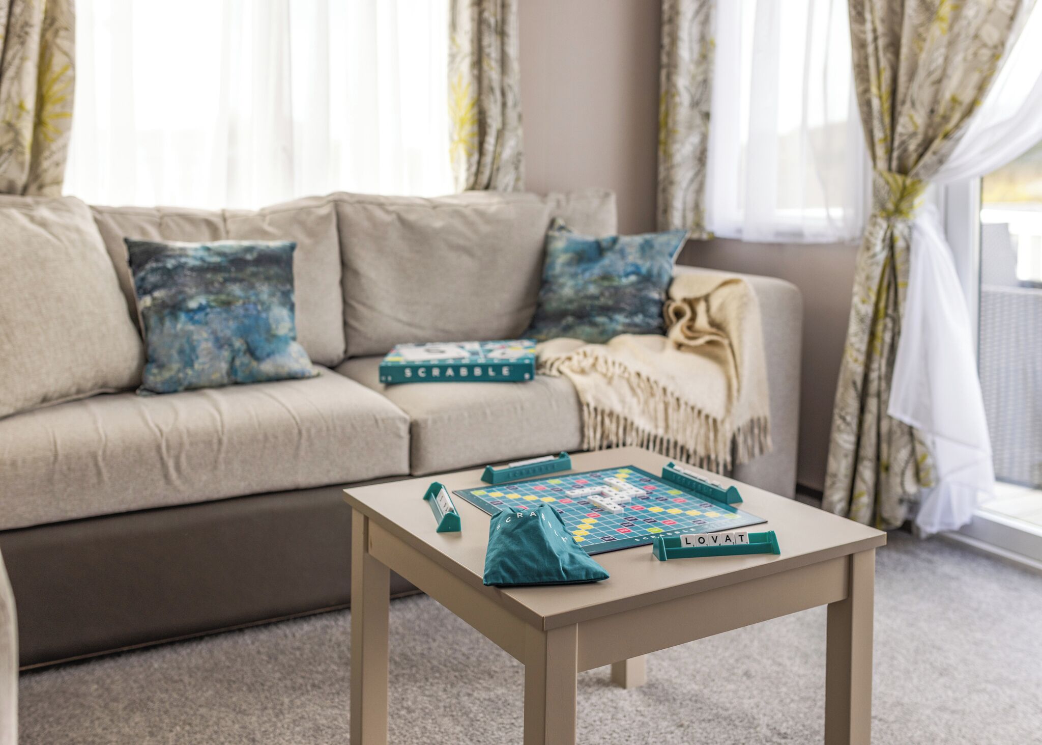 A living room with a sofa, a coffee table with a board game, and a blanket.