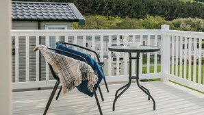 Un balcon avec une balustrade blanche, une table ronde et une chaise bleue recouverte d’une couverture.