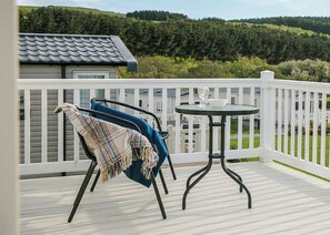 Un balcon avec une balustrade blanche, une table ronde et une chaise bleue recouverte d’une couverture.