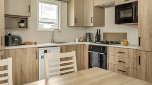 Une cuisine moderne équipée d’un lave-vaisselle, d’un grille-pain, d’une bouilloire, d’une cuisinière, d’un four à micro-ondes et d’une table à manger avec des chaises.