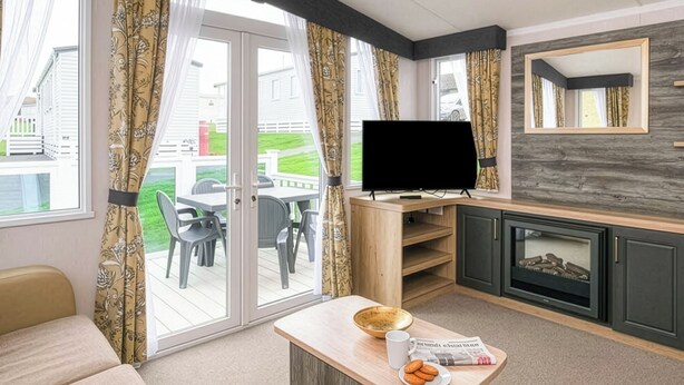 En moderne stue med et fladskærms-tv, pejs, spiseområde med stole og et stort vindue med gardiner.